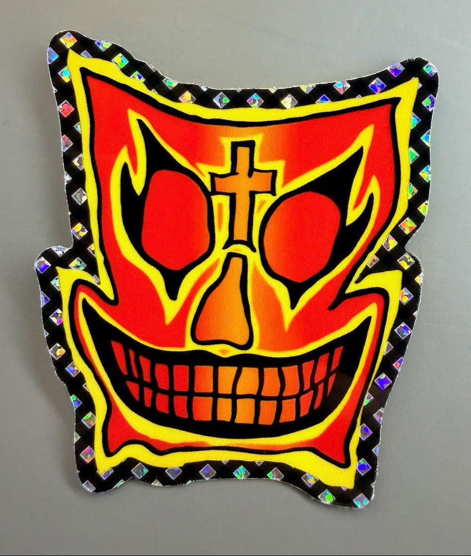 A die-cut John Grigley Pro Model Skateboard sticker featuring a stylized, fiery red and orange skull face with black outlines, a gold cross on the forehead, and a holographic diamond-patterned border, shown on a neutral gray background.