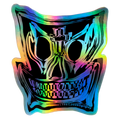A die-cut sticker featuring a stylized skull graphic with a holographic rainbow sheen, shown on a light gray textured background.