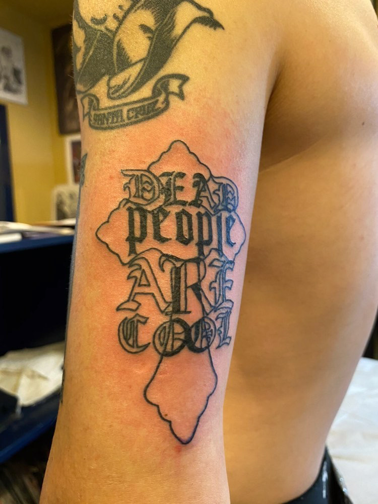 Tattoo on a person's arm with text and mountain design, with a blurred background.