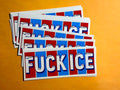 A stack of rectangular stickers with the word 'FUCK ICE' in large white letters over alternating red and blue vertical blocks, photographed on a solid orange background.