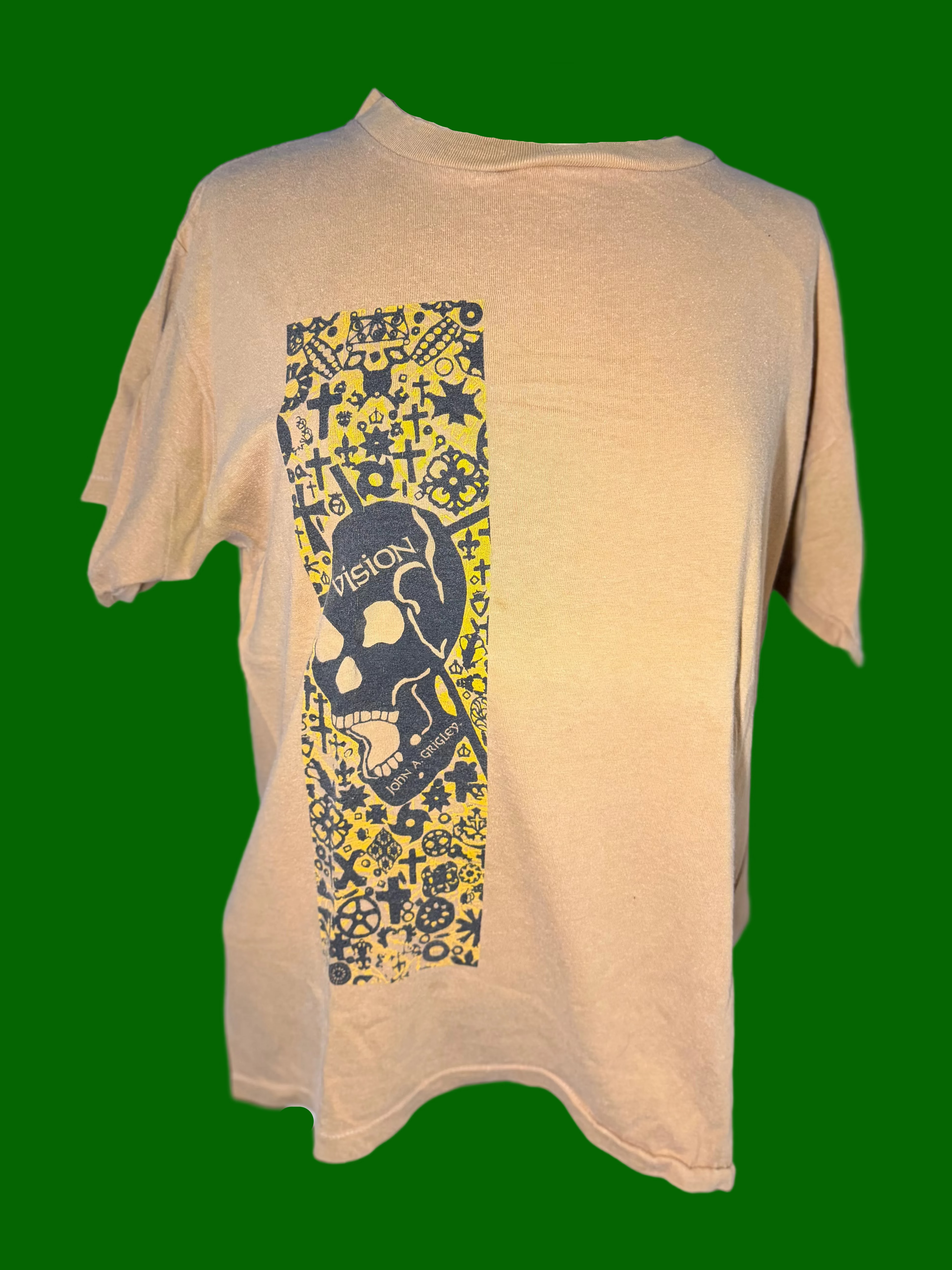 A mustard yellow short-sleeve t-shirt displayed on a mannequin torso, featuring a vertical graphic print on the front with a skull and the word 'VISION' surrounded by yellow graffiti-style patterns.