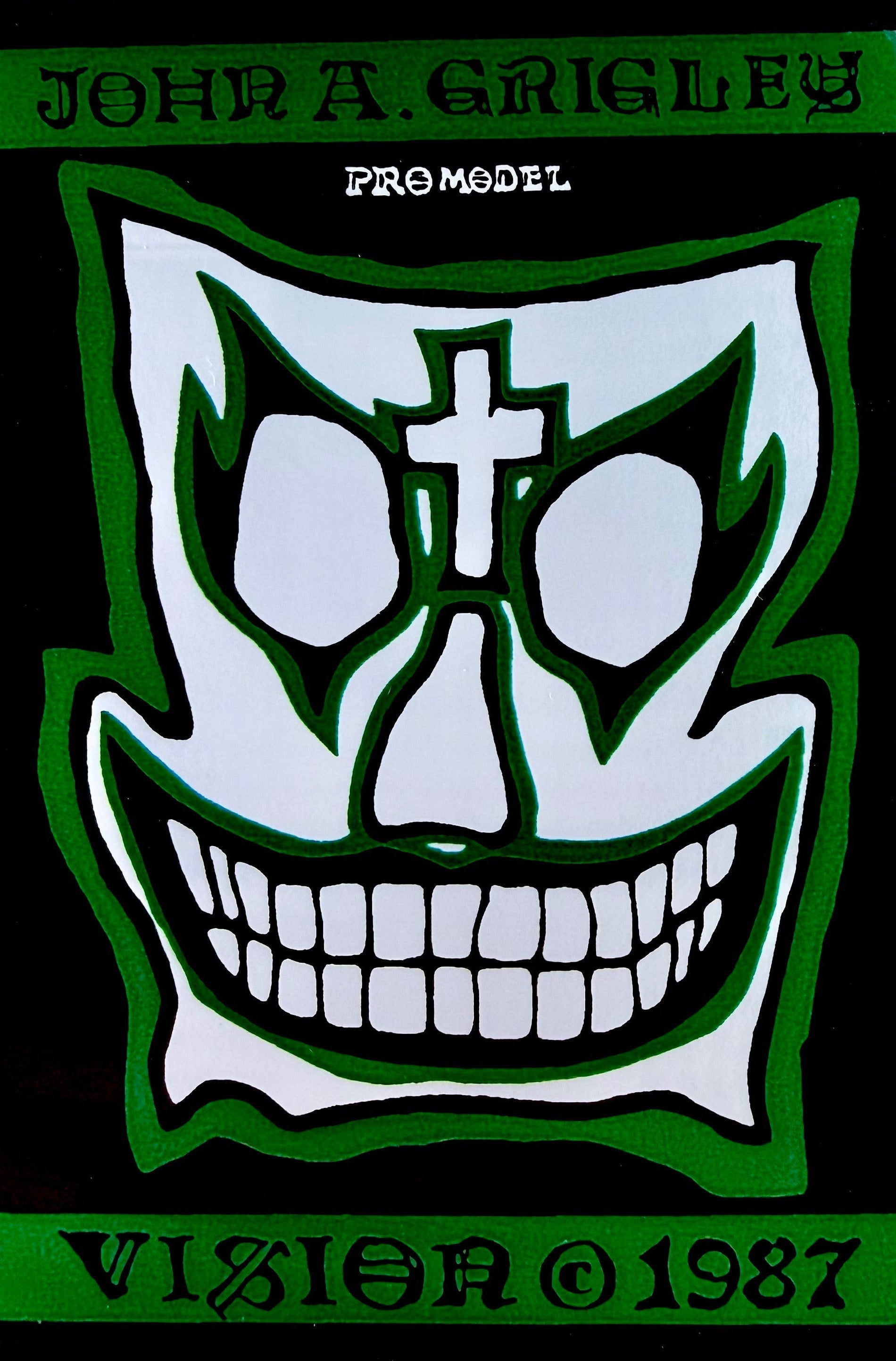 Skull design with cross and green border on a black background, featuring 'John A. Grigley' and 'Vision 1987'.