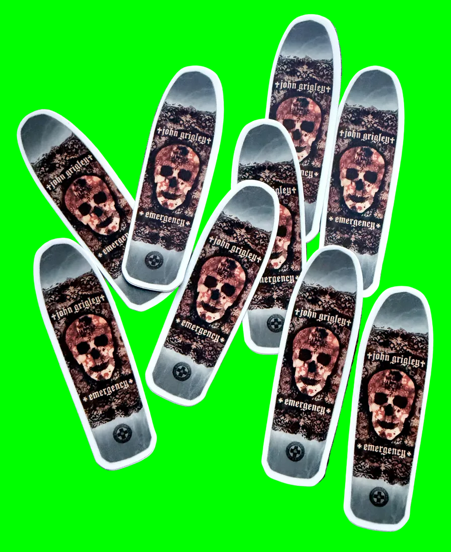 Nine skateboard decks arranged in a fan-like pattern on a dark, textured background. Each deck features a graphic design with a skull, the text 'john grigley', and 'emergency' with a small black circular emblem near the bottom.