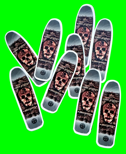 Nine skateboard decks arranged in a fan-like pattern on a dark, textured background. Each deck features a graphic design with a skull, the text 'john grigley', and 'emergency' with a small black circular emblem near the bottom.