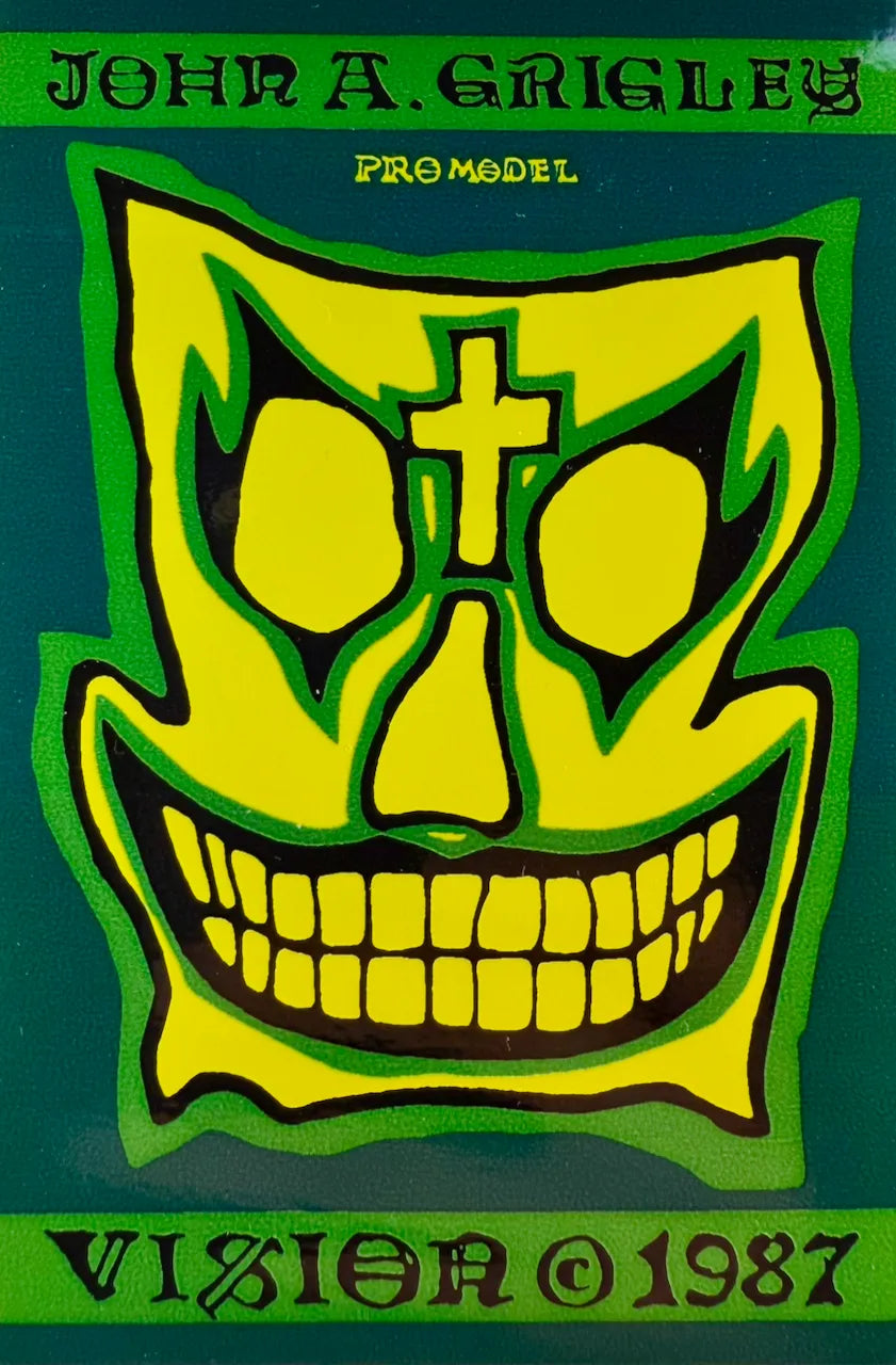 A graphic print or album cover featuring a stylized yellow skull face with a cross on its forehead, outlined in black against a dark green background. Text at the top reads 'JOHN A.