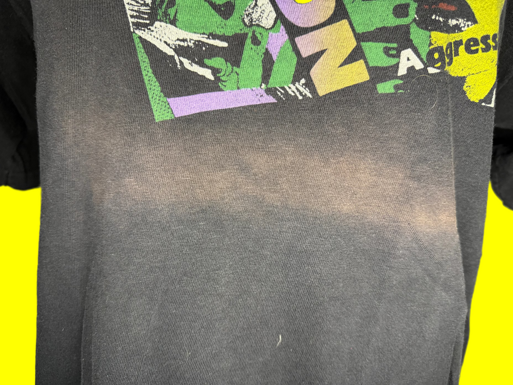 A close-up of a dark gray graphic t-shirt featuring a distressed, colorful print with green, yellow, and purple elements at the top, with a faded burn or heat-press effect across the center.
