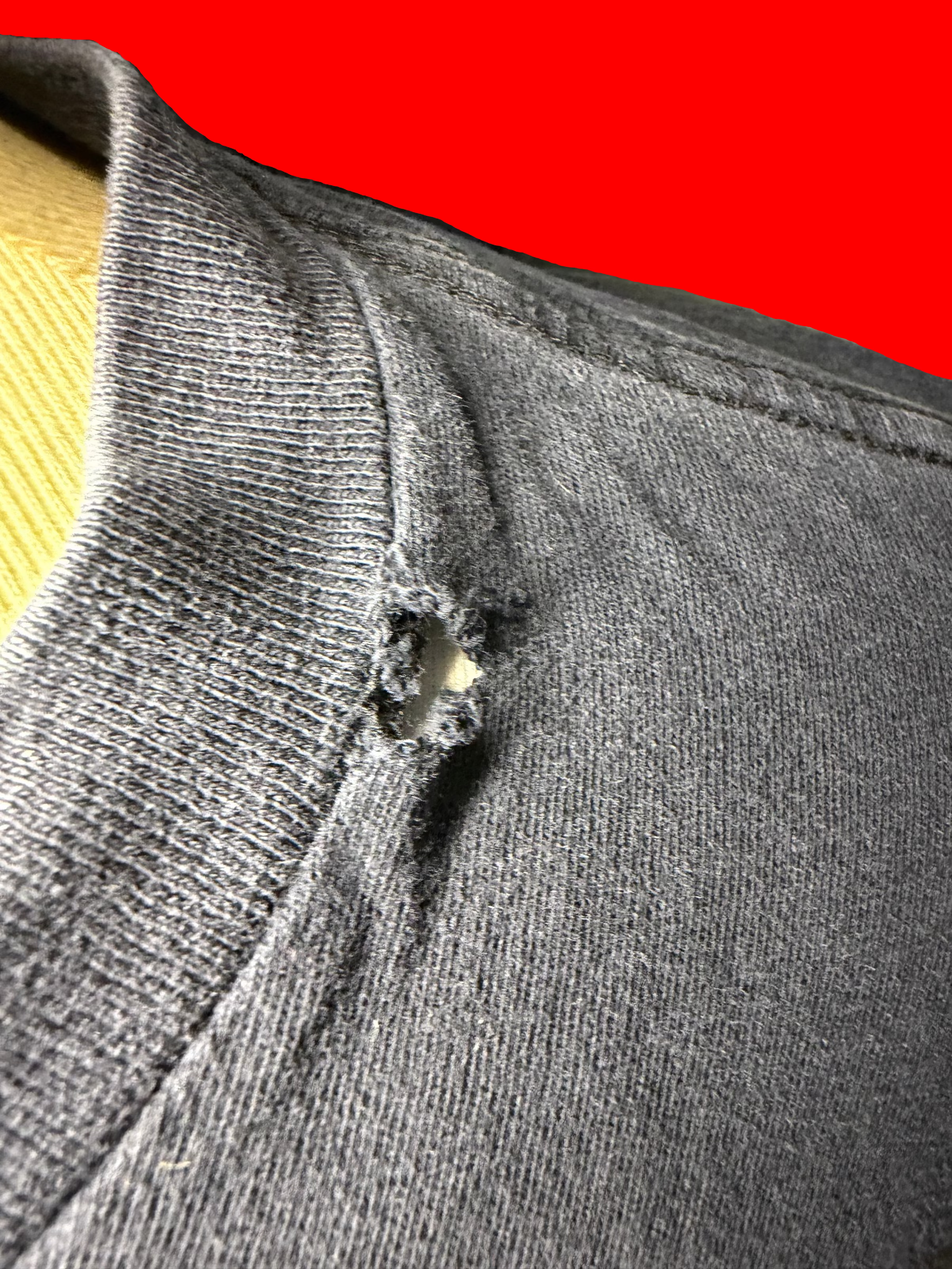 Close-up of a dark gray ribbed knit garment with a small hole near the collar, shown against a bright red background.