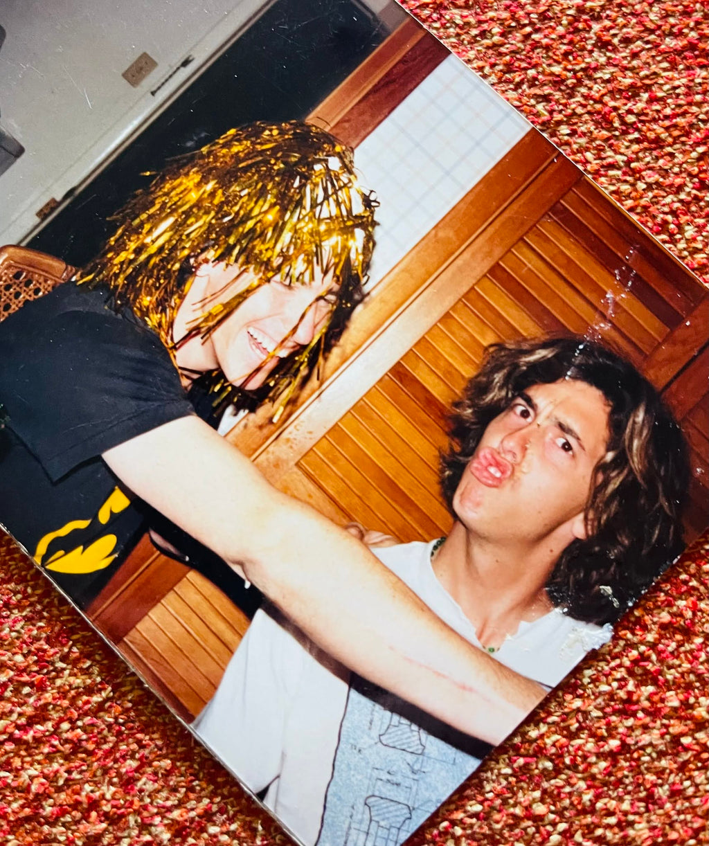 Two people sitting on a couch with a wooden floor and textured red and brown background.