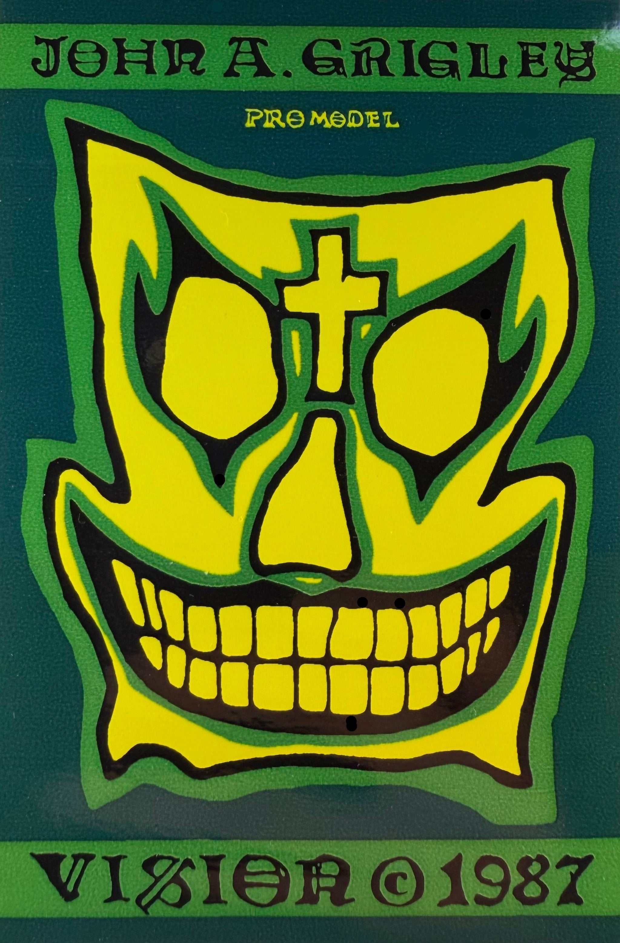 Skull design with cross on a green background, featuring text 'John A. Grigley', 'Promodel', and 'Vision 1987'.