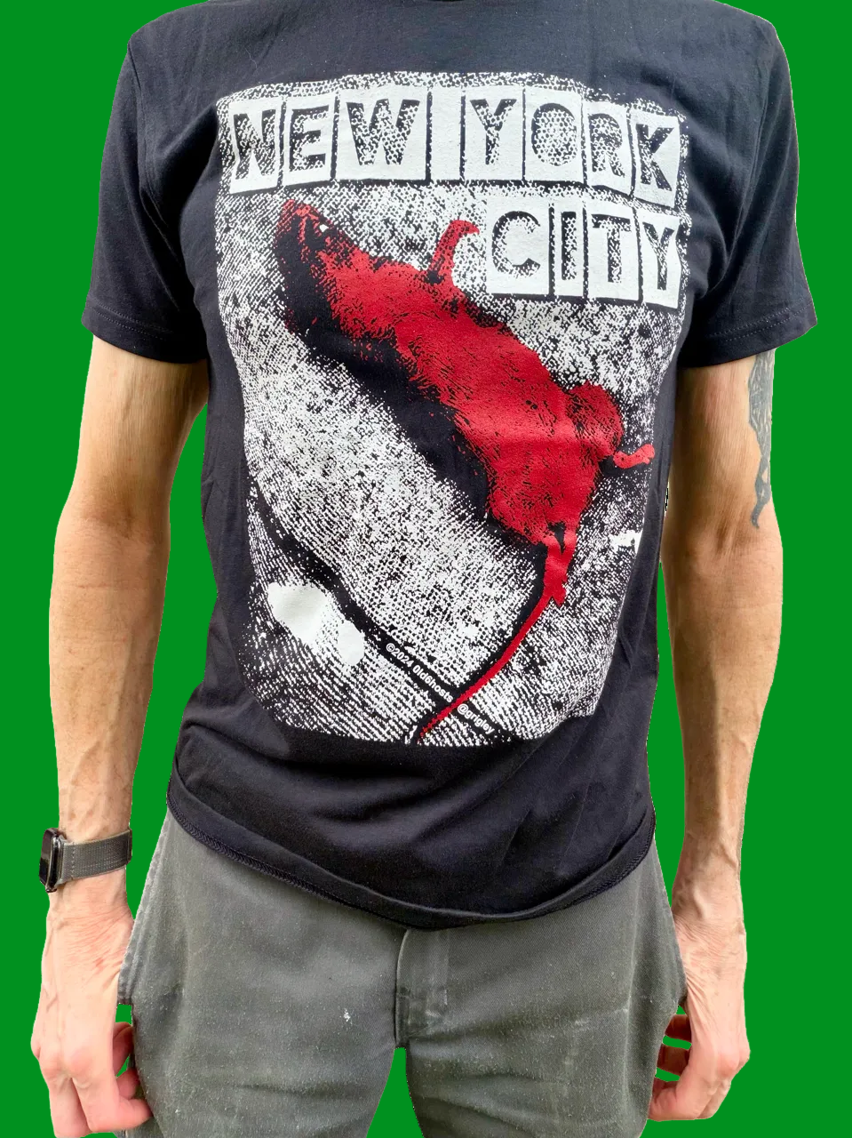 A man wearing a black graphic t-shirt with a distressed red and white print reading 'NEW YORK CITY' and a red DEAD RAT silhouette, paired with gray pants against a red background.