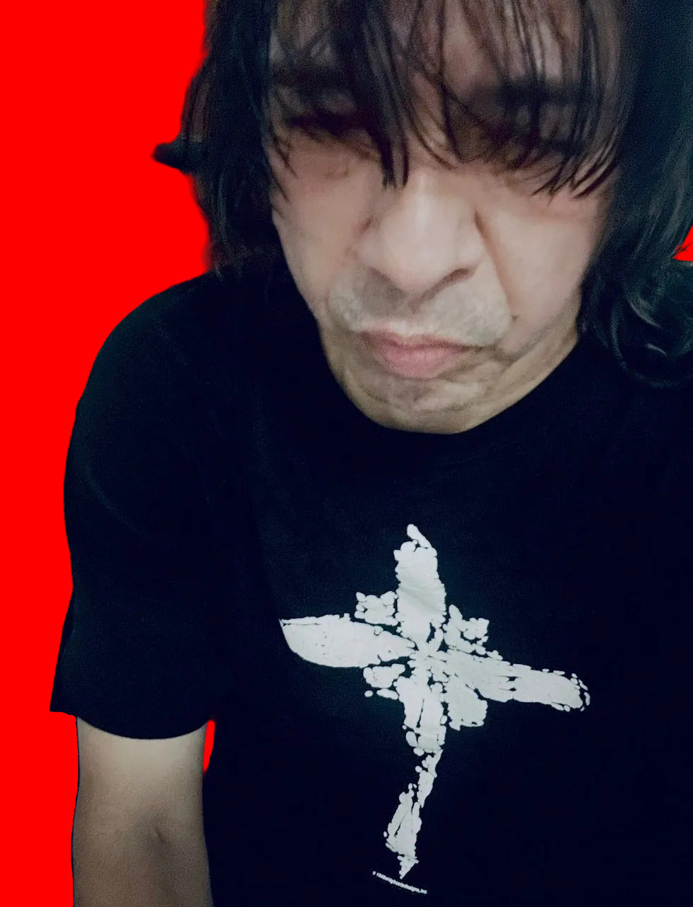 A close-up selfie of a man wearing a black t-shirt with a white distressed cross graphic on the front, looking down at the camera.
