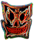 A mask-shaped 2026 new rendition of a 1987 John A. Grigley Pro Model Skateboard Decal with a black base and bold red, orange, beige, and white graphic lines, outlined in holographic glitter. The design includes a stylized face with large eye sockets, a cross motif above the nose, and a wide toothy grin.