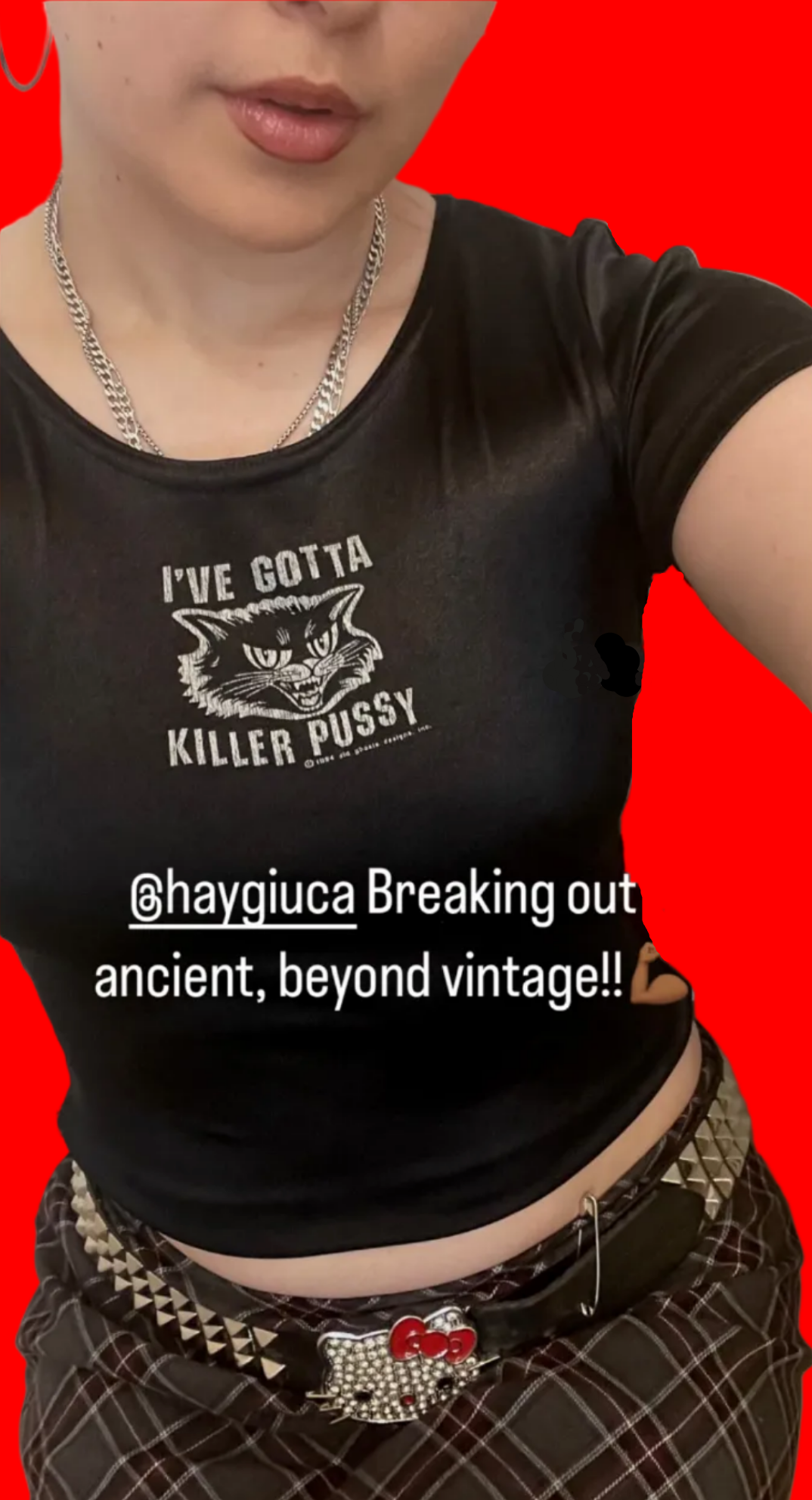 Person wearing a black t-shirt with GOTTA KILLER PUSSY and a belt with a heart buckle.