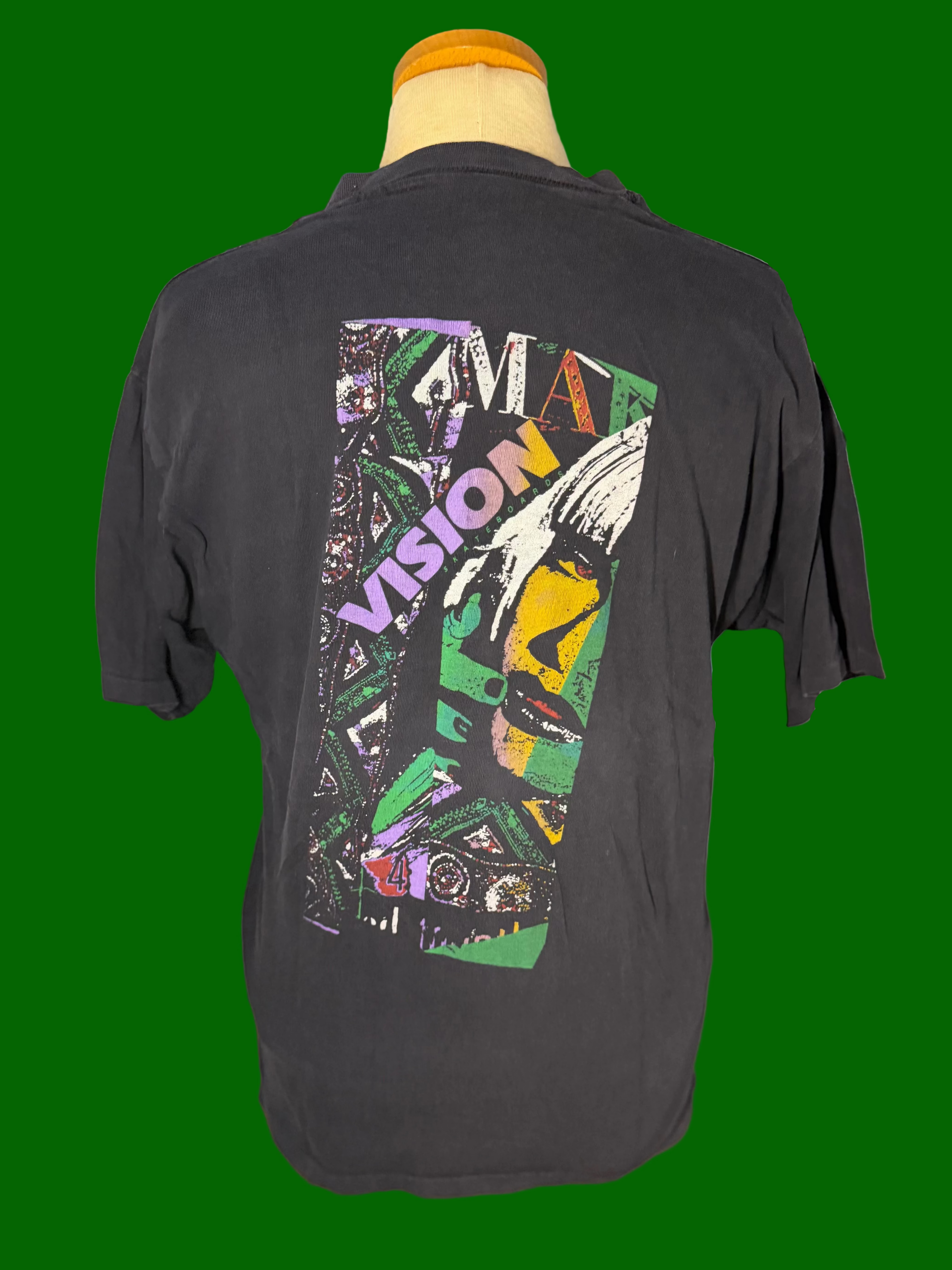 A faded black short-sleeve t-shirt displayed on a mannequin torso, showing a large multicolor graphic print on the back with the word 'VISION' and a stylized face.
