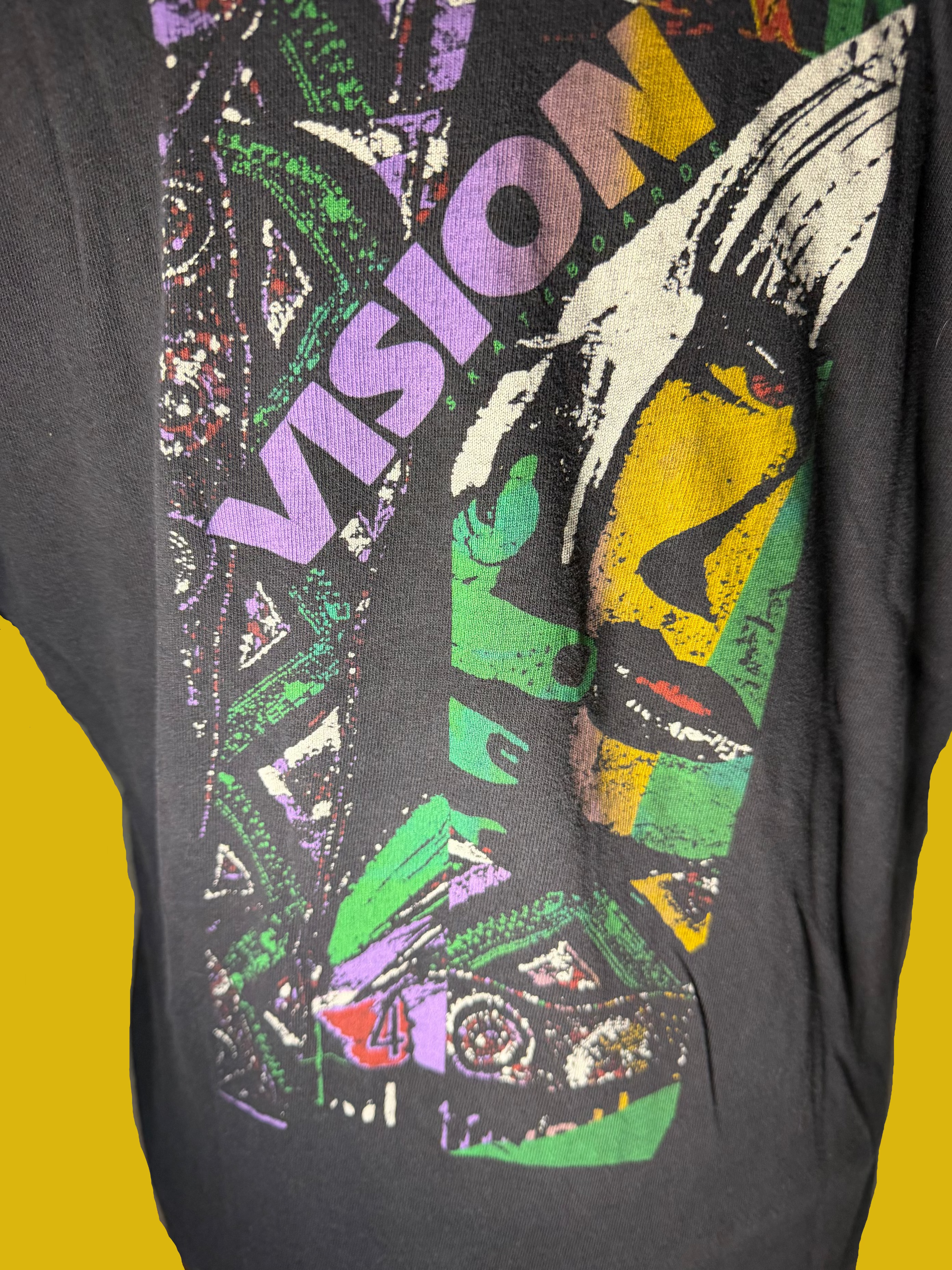 A close-up of a fded back graphic t-shirt featuring a vibrant multicolor print of the Vision logo and skateboard artwork.
